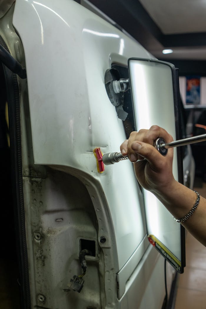 client-stories-img Close-up of vehicle dent repair in a garage using specialized tools under bright lighting.