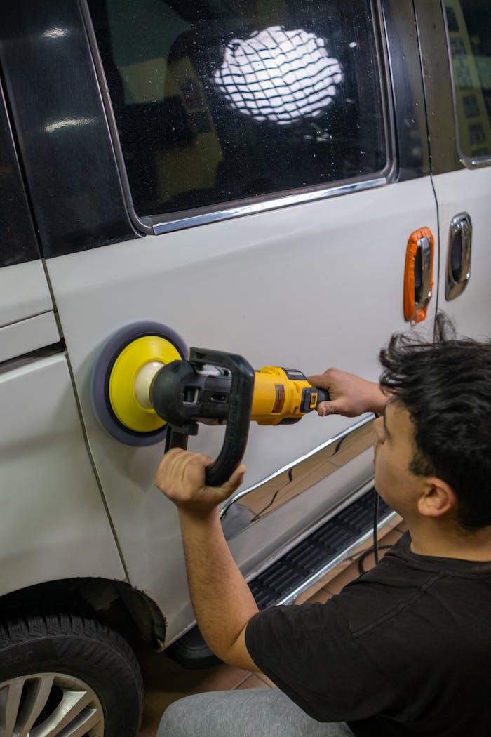 A person polishing a car with a buffer in an automotive repair workshop.